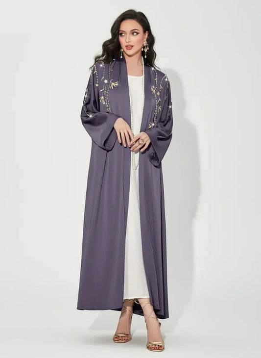 Femme portant un abaya violet orné de broderies dorées et robe blanche, chaussure à talon dorée