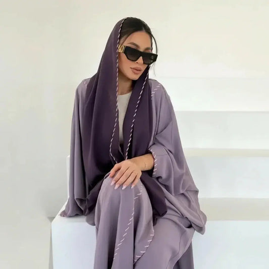 Femme élégante en abaya violet clair avec voilette foncée et lunettes de soleil noires dans un décor minimaliste