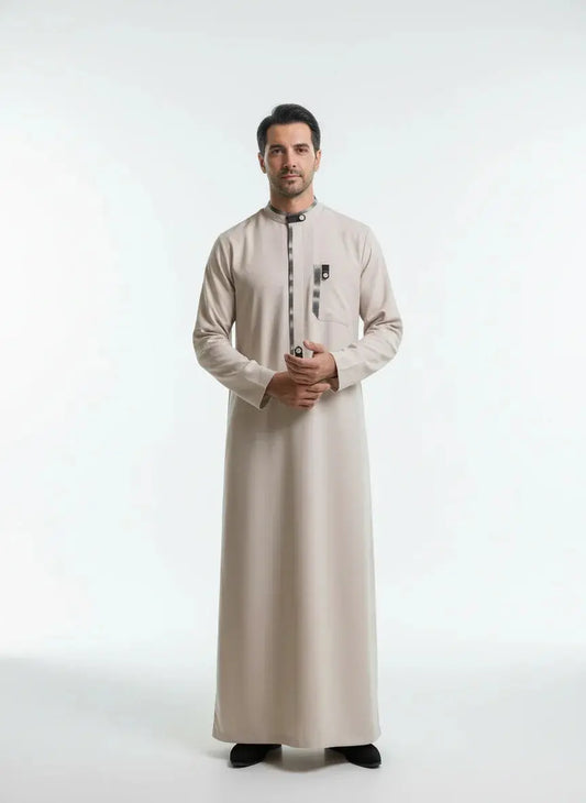 Homme portant une thobe beige clair avec détails noirs, debout sur fond blanc minimaliste