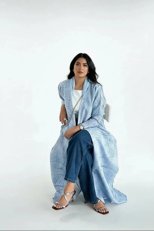 Femme assise en long cardigan bleu clair à motifs, jean bleu et sandales à talons argentées