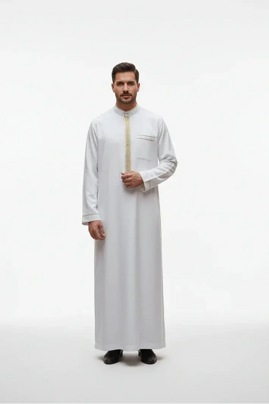 Homme portant une thobe blanche traditionnelle avec motifs dorés, chaussures noires, fond clair