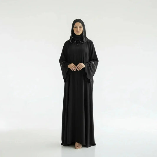 Femme portant un abaya noir avec broderies blanches sur manches et capuche, fond blanc minimaliste